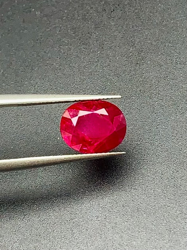 Ruby gemstone held between tweezers on a gray background