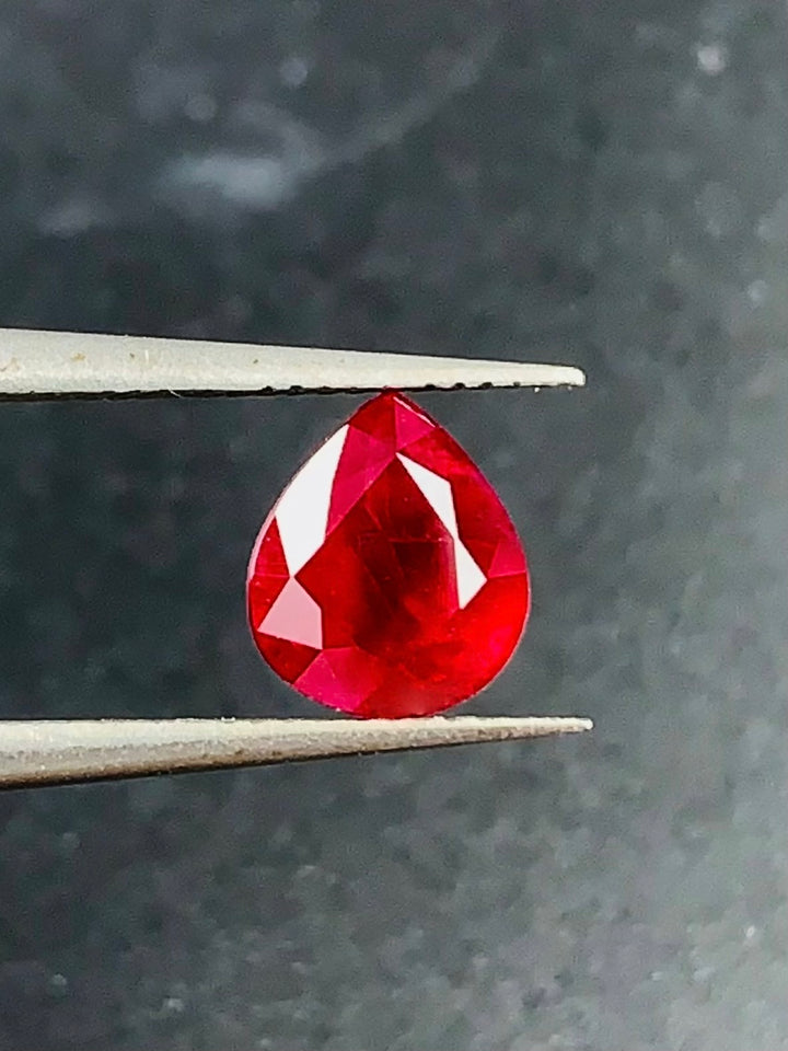 Teardrop-shaped Burma Ruby gemstone held between tweezers on a dark background
