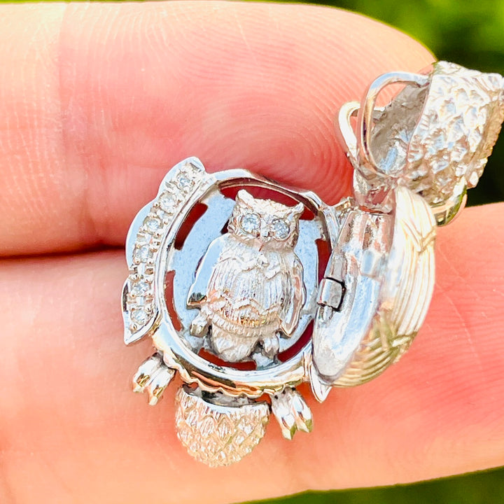 Silver and gold owl pendant held between fingers with a blurred green background